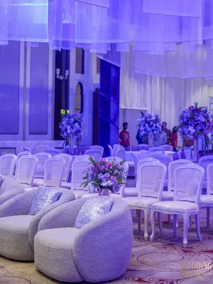 The guest seating for the ceremony, featuring elegant white chairs and plush, modern armchairs. The entire space is bathed in a soft lavender light, creating a serene and cohesive look.