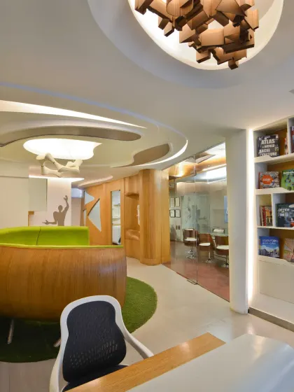 The reception desk in my studio is highlighted by a custom light fixture made of abstract wooden blocks. Opposite the desk, a bookshelf showcases our firm's projects, offering visitors a glimpse into our diverse portfolio.