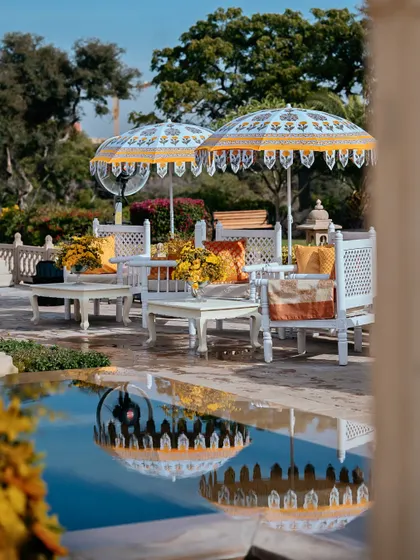 The poolside Haldi setup at Oberoi Udaivilas, with elegant white furniture and block-printed umbrellas reflecting in the water.