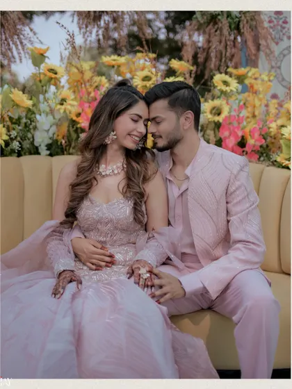 A tender moment between the couple, seated on a yellow couch against a backdrop of sunflowers. This intimate shot perfectly captures their connection amidst the vibrant decor of their Haldi carnival.