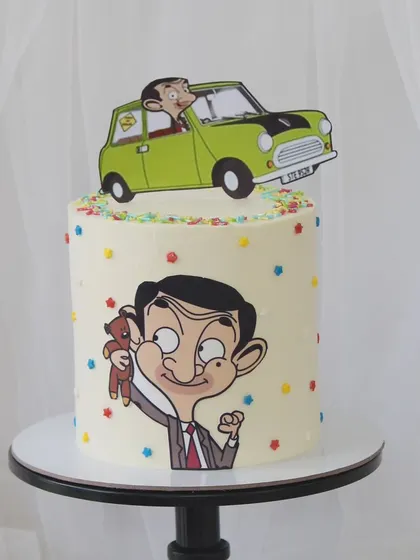 A fun and nostalgic Mr. Bean cake. This design features edible prints of the beloved character and his iconic green Mini, decorated with colorful sprinkles for a cheerful touch.