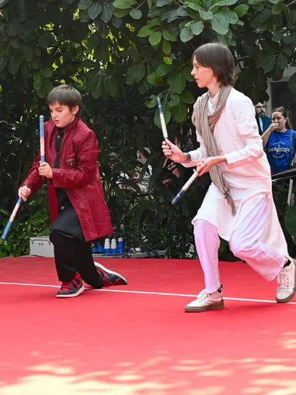 Two boys performing a traditional stick dance on a red carpet at the Charity Mela. We celebrate a fusion of cultures, blending Indian and French traditions in our events.