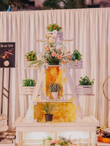 A decorative food station setup. We used a white ladder shelf adorned with flowers and greenery to create a charming, rustic display area next to the main buffet.