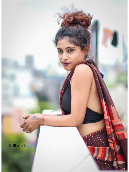 A modern and edgy take on a saree portrait, shot on a rooftop with the city skyline blurred in the background.