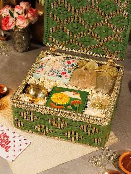 A closer look at our green and gold woven Diwali hamper. It includes a beautiful urli, aromatic tea pouches, and other festive treats, all nestled in a reusable basket.