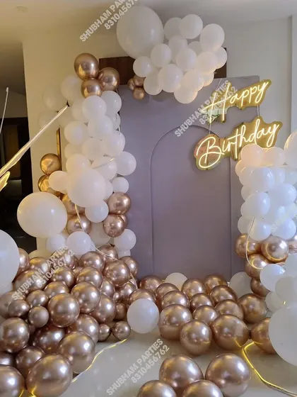 A sophisticated white and rose gold balloon arrangement with a large butterfly prop and neon sign.