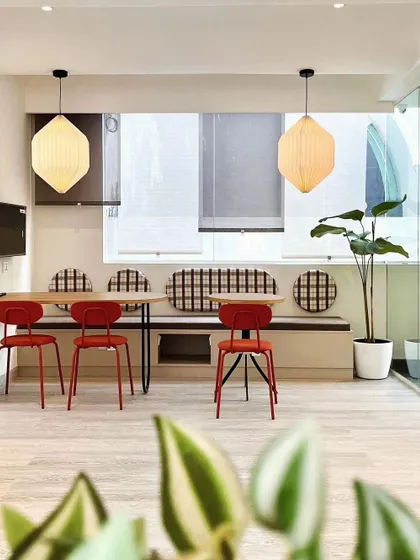 A vibrant dining space with red chairs and a comfortable bench seat, illuminated by large hexagonal pendant lights.