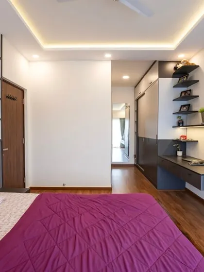 This modern bedroom features smart storage with floating shelves and a built-in desk, complemented by a geometric accent wall and a rich wooden bed frame.