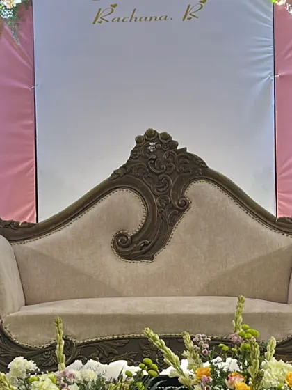 An elegant carved sofa for the main seating at a traditional ceremony, framed by a simple backdrop and fresh flower arrangements.