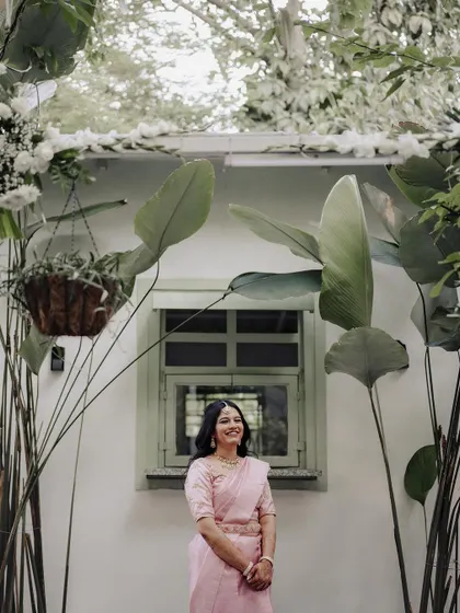 A lovely portrait of a guest or family member in a beautiful pink saree. The natural green backdrop and soft lighting create a fresh and elegant look.