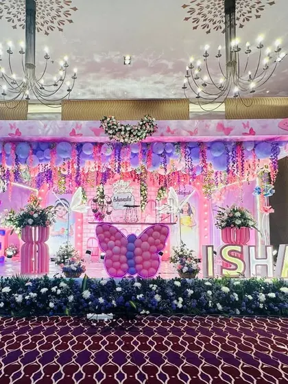 A grand stage setup for a butterfly-themed first birthday, with a canopy of hanging flowers and balloons, and large light-up butterfly props.
