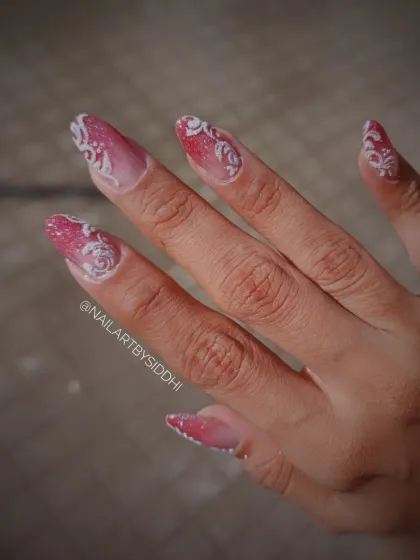 A romantic bridal set featuring a glittery red-pink ombre base with intricate, hand-painted white scrollwork.