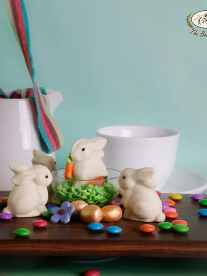 Our 'Bunny in a Globe' is a whimsical Easter treat. This image shows our adorable, handcrafted white chocolate bunnies nestled in a bed of green frosting, ready to delight.