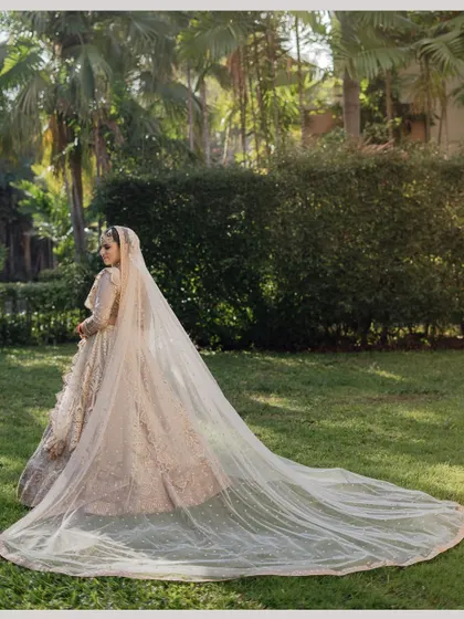 The bride's magnificent long veil trails behind her as she walks through the lush green lawns of the resort.