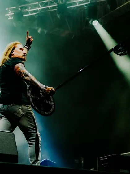 A powerful shot of a Dream Theater band member commanding the stage, raising his instrument to a roaring crowd.