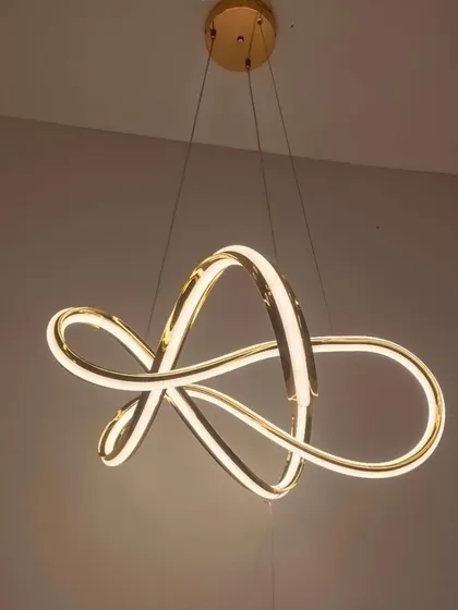 An abstract ribbon-style chandelier in a gold finish. The flowing, continuous loop of light creates a sense of motion and artistry.
