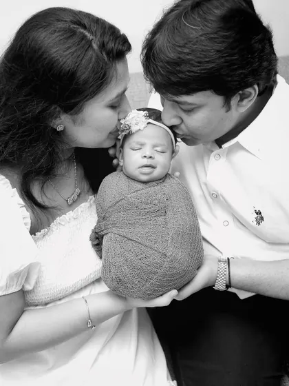 A timeless black and white portrait of parents kissing their newborn's head. This classic pose emphasizes the love and protection surrounding the newest family member.