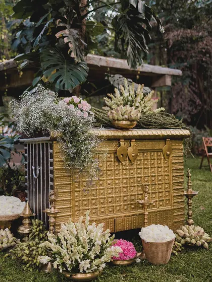 An antique gold-finished chest serves as a stunning decorative piece, overflowing with tuberose and baby's breath. This element combines vintage charm with floral elegance, creating a beautiful focal point in the garden setting.