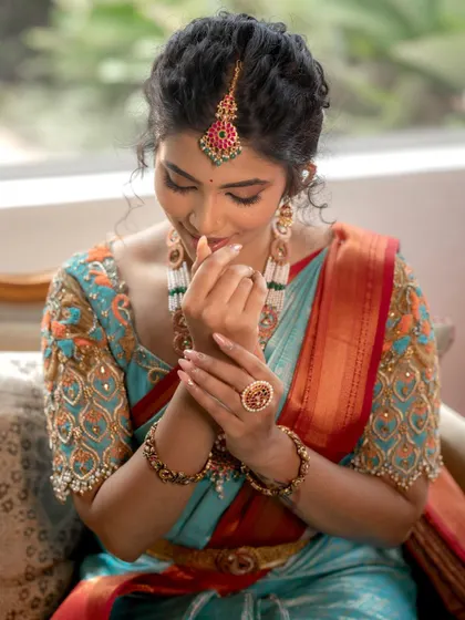 A close-up of the hand and jewelry details. The makeup is designed to complement the overall look, including the accessories.