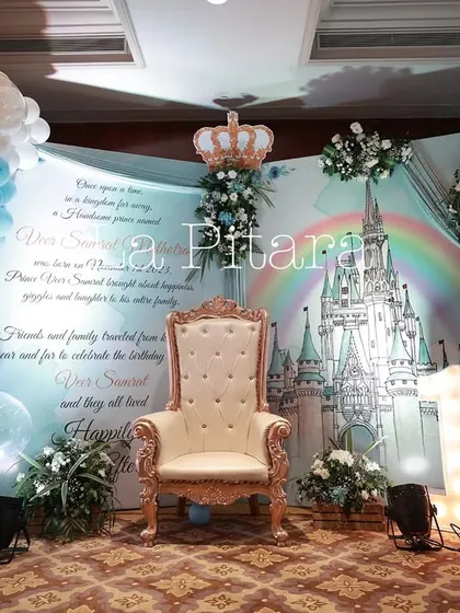 The royal photo stage featured a throne fit for a prince, set against a backdrop telling a fairytale story. Balloon arches in blue and gold, along with a castle illustration, completed the majestic scene.