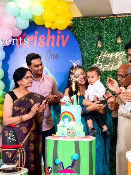 A family celebrating their son's first birthday with a Cocomelon-themed cake cutting.