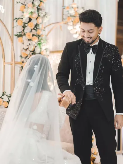 A sweet moment during the ring ceremony. The groom holds the bride's hand, his expression full of love and admiration as she looks down with a smile.