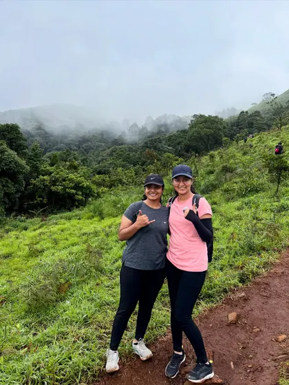 Enjoying the view of the misty, forest-covered hills from the Bandaje trek trail. The landscape is a stunning mix of green meadows and dense shola forests.