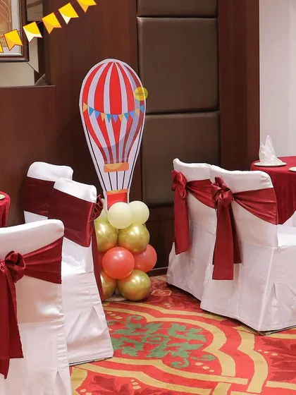 Details from the carnival-themed birthday, including hot air balloon cutouts and chairs decorated with festive red bows, helping to carry the theme throughout the entire venue.