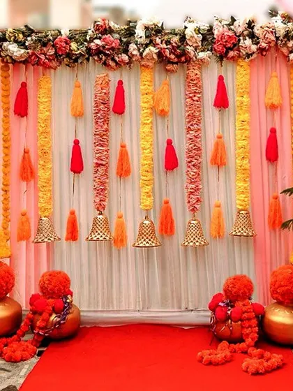 A beautiful backdrop for a home ceremony, using drapes, marigold garlands, and tassels. This kind of setup is perfect for creating a dedicated photo area or for the main ritual.