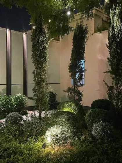 The right lighting can transform a garden at night. For this high-end farmhouse project, I used strategic uplighting to highlight the form of cypress trees and manicured shrubs, creating a dramatic and elegant evening ambiance.