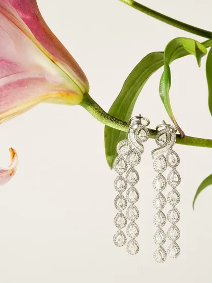 A pair of magnificent cascading diamond earrings hangs delicately from a lily stem. This creative composition emphasizes the jewellery's elegance and connects it with natural beauty.