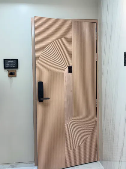A beautiful safety door with a fluted, rose-gold finish and a smart lock. The concentric curved pattern adds a soft, artistic touch.
