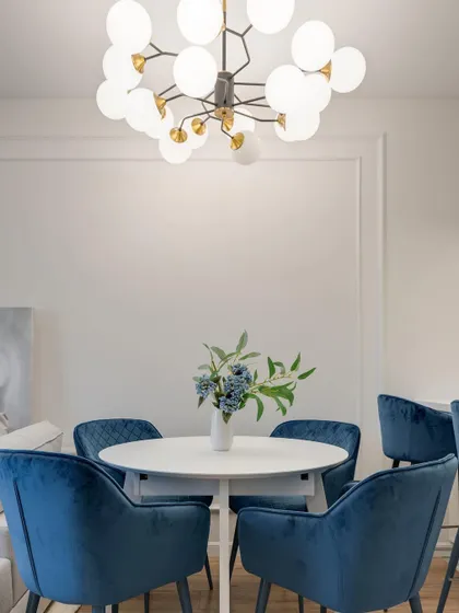 A dining setup featuring royal blue velvet chairs around a simple white table, creating a look of modern elegance. The bubble chandelier adds a touch of playful sophistication.