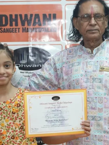 A senior guru proudly stands with his young student and her award. This image captures the passing of knowledge and tradition from one generation to the next.