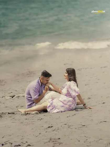 A tender moment on a sandy beach, with the groom kissing his bride's hand as they sit by the water.