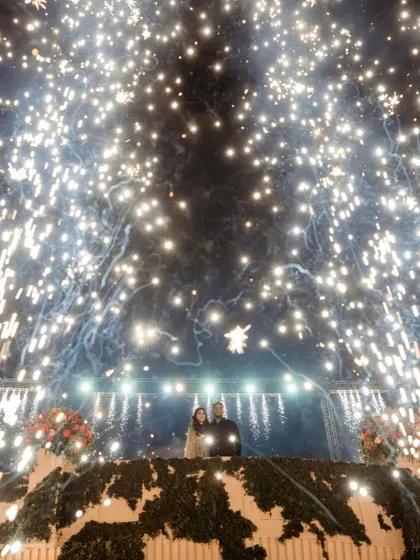 A shower of pyrotechnics rains down as the couple stands on the bridge, creating a magical and celebratory atmosphere.