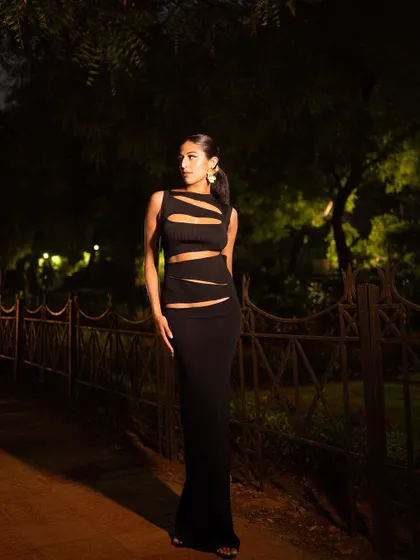 A classic fashion pose against a dark, natural background. The lighting is carefully controlled to make the model and her outfit the central focus, creating a timeless and elegant image.