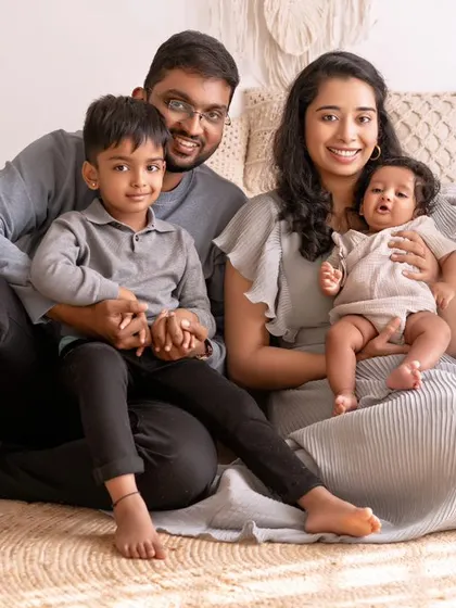 A beautiful family of four seated together in my studio. The older brother holds his parents' hands while the mother cradles the new baby, a perfect portrait of a growing family.