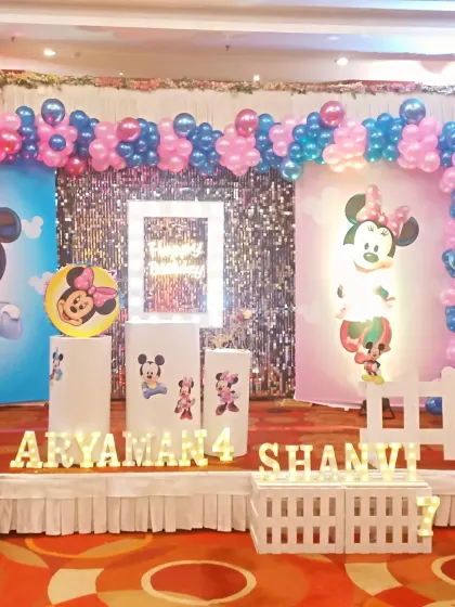 A clear shot of the birthday stage elements, including the character-themed pedestals and the illuminated names and ages of the children, 'Aryaman 4' and 'Shanvi 7'.