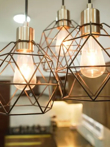 A close-up of the geometric pendant lights hanging over the kitchen counter. These fixtures add a modern, decorative element to the warm, metallic tones of the cabinetry.