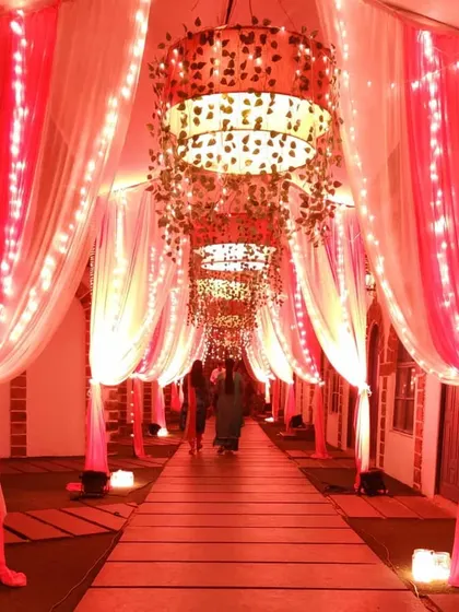A beautiful passage design with alternating pink and white drapes and fairy lights. The large, custom-made chandeliers add a unique and grand element to the walkway.