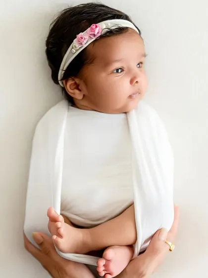 A newborn is held securely in a white wrap, a simple and classic pose that highlights the baby's delicate features.