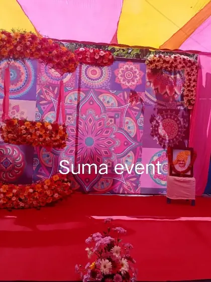 A vibrant naming ceremony stage featuring a large crescent-shaped swing completely covered in red and orange marigolds. The colorful patterned backdrop makes the entire setup feel festive and joyful.