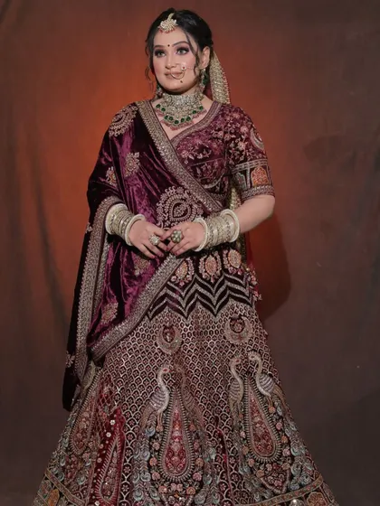A full-length view of a deep wine-colored velvet lehenga. The intricate peacock embroidery makes this a unique and regal choice for a winter bride.