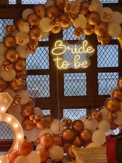 Another angle of the gold and white bachelorette party decor, highlighting the "Bride to be" neon sign and the full balloon arch.