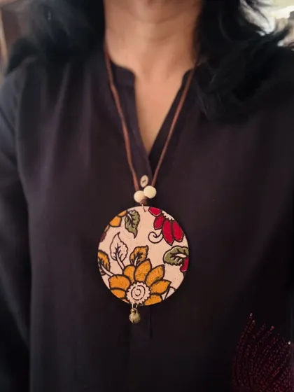 A simple yet elegant pendant made with a piece of floral Kalamkari fabric. The neutral background and earthy colors make it a versatile accessory for any kurta or top.