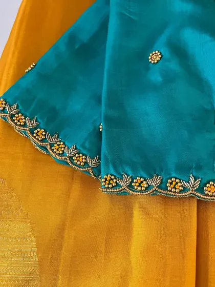 A close-up of the sleeve of a teal blue blouse. The scalloped border is created with beautiful beadwork in yellow and gold, with small floral butis scattered across the sleeve.