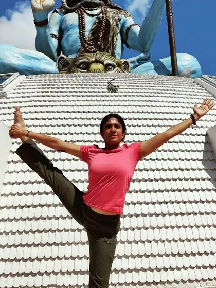 A standing leg extension pose, or Utthita Hasta Padangusthasana, in front of a magnificent statue of Lord Shiva in Nepal.