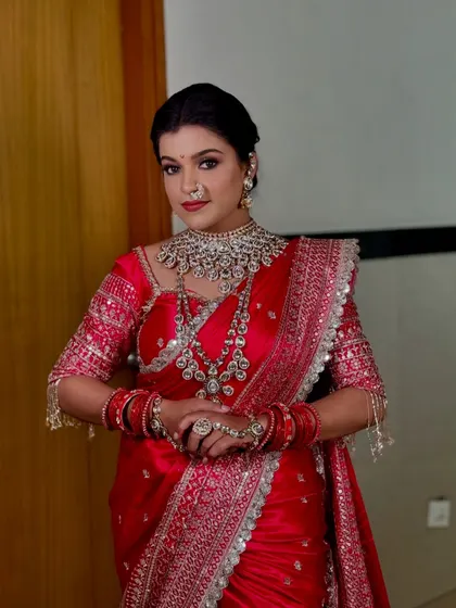 A powerful bridal portrait in a red saree with heavy silver embroidery. The drape is structured to showcase the intricate work on the blouse and pallu.