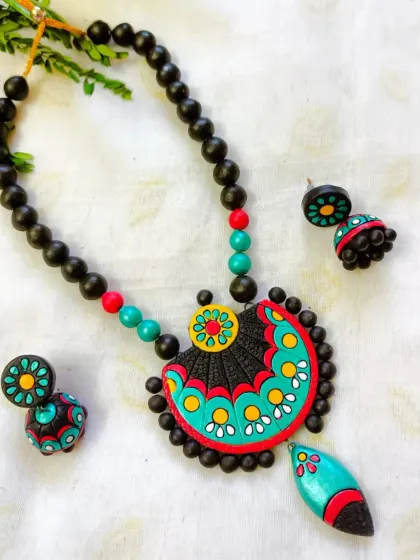 A semi-circular pendant necklace with a fan-like design in turquoise and red. The set includes matching jhumkas and is available in many colors.